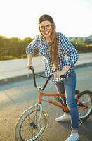 charmant Jeune femme dans une chapeau équitation une vélo sur ville Contexte dans le lumière du soleil Extérieur photo