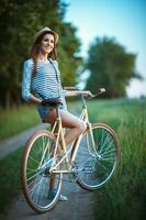 charmant Jeune femme dans une chapeau avec une vélo dans une parc photo