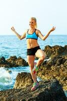 athlétique femme relaxant - pratiquant yoga sur le rochers par le mer photo