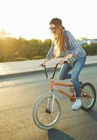 charmant Jeune femme dans une chapeau équitation une vélo sur ville Contexte dans le lumière du soleil Extérieur photo