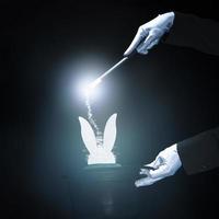 Magicien effectuant un tour avec baguette magique sur fond noir brillant photo