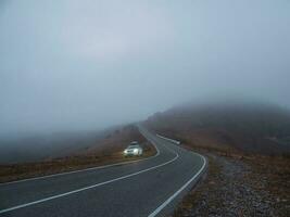 une vagabond voiture suv avec brouillard lumières tourné sur est garé suivant à une scénique route route dans une brumeux l'automne paysage. bagage tronc boîte Montagne sur voiture toit étagère. photo