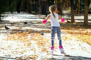 peu fille sur rouleau patins et tram protection équitation dans le l'automne parc. en bonne santé mode de vie concept. photo
