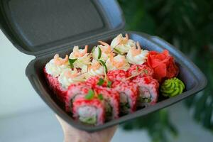 une ensemble de Sushi et Rouleaux dans une noir boîte décoré avec micro-pousses. nourriture livraison. Californie Rouleaux avec crevette. photo