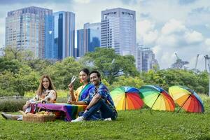 groupe de transgenres et homosexuel gens à votre santé et célébrer lgbtq fierté mois dans coloré robe et arc en ciel drapeau tandis que pique-nique à l'intérieur le parc photo