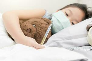 malade fille pose sur lit et en portant thermomètre dans main photo