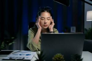 fatigué Jeune femme cache yeux avec mains à portable PC en retard dans le soir. photo
