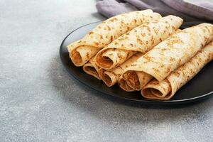 mince Crêpes roulé dans une rouleau sur une plaque. le concept de une délicieux petit déjeuner ou maslenitsa. béton Contexte. photo