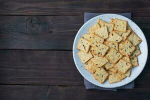 De délicieux biscuits craquelins sains avec des graines de lin et des graines de sésame sur une assiette. fond d'une collation saine, table en bois rustique sombre. espace de copie. photo