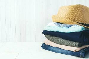 une empiler de aux femmes Vêtements et une paille chapeau sur blanc planches avec une copie de espace. photo