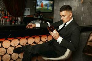 Beau Jeune homme dans une élégant costume en portant une bouteille de whisky à le bar. photo