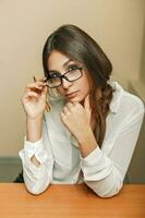 Jeune magnifique femme avec des lunettes séance à le tableau. photo