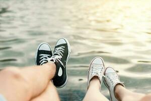 Jeune couple mensonge sur le plage. jambes avec baskets près l'eau photo