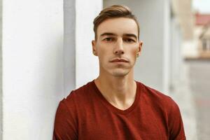 portrait de une Jeune Beau homme avec une la Coupe de cheveux dans une gilet près une blanc mur photo