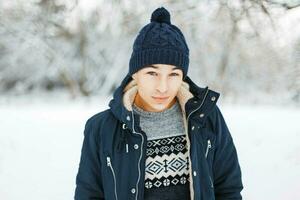 Beau Jeune homme dans hiver veste, tricoté chandail avec une modèle et une tricoté chapeau en marchant dans une hiver parc photo