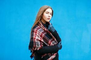 Jeune femme avec une à carreaux rouge écharpe près une bleu mur photo