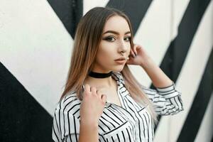 jolie femme dans une blanc chemisier avec noir rayures près le mur avec lignes. boucle d'oreille dans le nez photo