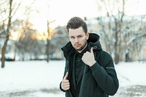 Beau Jeune homme modèle avec cheveux dans une noir veste dans une neigeux parc photo