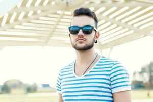 Beau branché homme avec barbe dans des lunettes de soleil sur une ensoleillé journée à le plage. photo