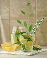 limonade dans une transparent verre avec citron, chaux, Romarin brins et menthe feuilles sur une blanc Contexte photo