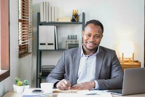 un africain américain homme d'affaire dans une noir costume souriant et montrant joie à le de l'entreprise annuel profit à construire confiance pour les clients qui volonté investir dans le bureau. photo