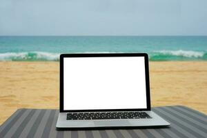 portable avec Vide écran pour Créatif conception sur plage lit proche plage et bleu mer Contexte. ordinateur carnet avec coupure chemin pour présent atterrissage page conception moquer en haut modèle photo