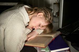 une fatigué étudiant est tombée endormi sur une livre près le ordinateur à nuit. photo