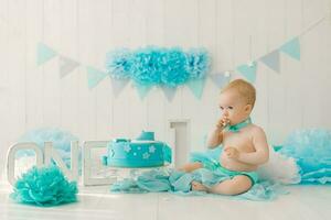 anniversaire fête pour une Un an garçon dans bleu et turquoise guirlandes et une gâteau, vacances concept et décor, une enfant avec une gâteau photo