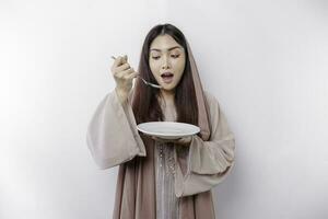 une souriant asiatique musulman femme est jeûne et faim et en portant et montrer du doigt à une assiette photo