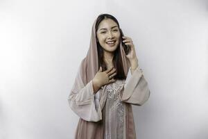 une content asiatique musulman femme portant une foulard, Heureusement parlant sur le téléphone, isolé par blanc Contexte photo