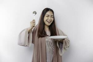 une souriant asiatique musulman femme est jeûne et faim et en portant et montrer du doigt à une assiette photo