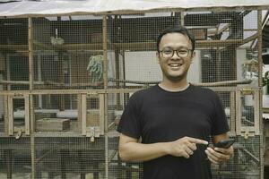 Beau asiatique homme est souriant et permanent dans de face de oiseau cage photo