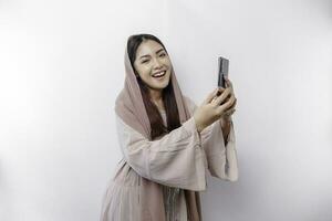 une content asiatique musulman femme portant une foulard, en portant sa téléphone, isolé par blanc Contexte photo