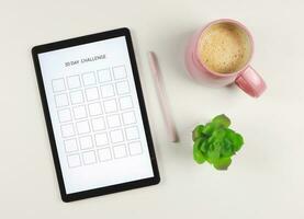 plat allonger de numérique tablette avec modèle 30 journée défi sur filtrer, rose style stylo, café et succulent plante pot isolé sur blanc Contexte. photo