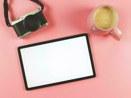 plat allonger de numérique tablette avec Vide blanc écran , numérique caméra et rose tasse de café isolé sur rose Contexte. photo