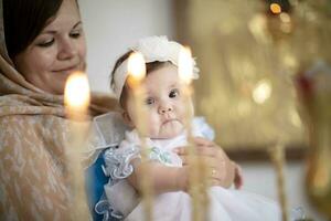 Baptême de le enfant.l'enfant nouveau née avec le sien mère dans le église parmi le bougies photo