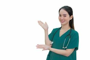 professionnel asiatique femme médecin dans vert uniforme des stands et sourit tandis que montrer du doigt à le Haut sur blanc Contexte. photo