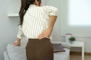 Asie magnifique femme en portant sa inférieur retour tandis que et souffrir de insupportable douleur santé et problèmes, chronique retour douleur, mal au dos dans Bureau syndrome, scoliose, hernie disque, muscle inflammation photo