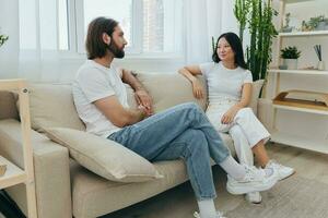 homme et femme copains séance sur le canapé et souriant joyeusement parlant à chaque autre ayant une bien temps ensemble. mode de vie dans bonheur à Accueil photo