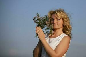 magnifique âge moyen blond avec une bouquet de fleurs sauvages contre le bleu ciel. photo