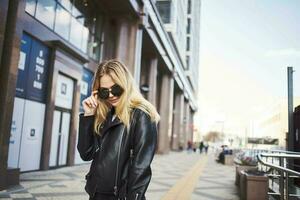 à la mode femme dans une cuir veste et des lunettes de soleil près le bâtiment photo