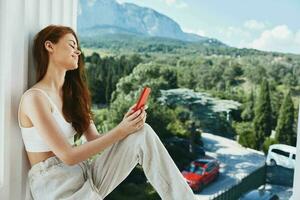 attrayant Jeune femme séance sur le balcon avec téléphone magnifique Montagne vue été inchangé photo