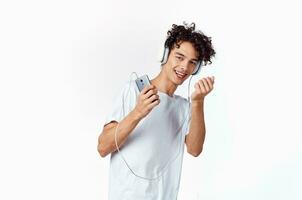 émotif gars avec frisé cheveux dans écouteurs écoute à la musique amusement photo