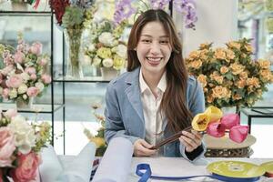 un Jeune magnifique asiatique femelle fleuriste ouvrier organiser et décorer bouquet de Frais fleurs, Valentin ordres, souriant avec content travail dans coloré Ralentissez boutique, petit affaires pme entrepreneur. photo