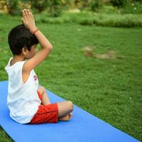 asiatique intelligent enfant Faire yoga pose dans le société parc Extérieur, enfants yoga pose. le peu garçon Faire yoga et méditation exercer. photo