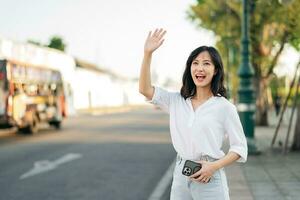 portrait Jeune magnifique asiatique femme agitant main à ami par le rue dans ensoleillé vacances. photo