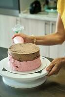 femme fabrication Chocolat gâteau avec rose crème, fermer. gâteau fabrication processus, sélectif concentrer photo