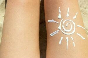 femme bain de soleil sur le plage avec une dessin de Soleil sur sa jambe avec crème photo