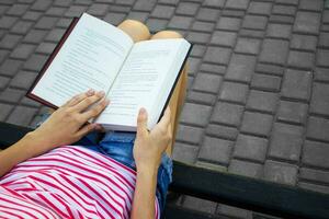 Haut vue de une Jeune fille en train de lire une livre. le fille est séance sur une parc banc et en train de lire une livre. photo