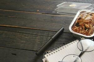 banane gâteau sur une noir en bois table avec Remarque livre, lunettes, et café tasses. photo